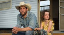 A white man and a young white girl sit outside a home.