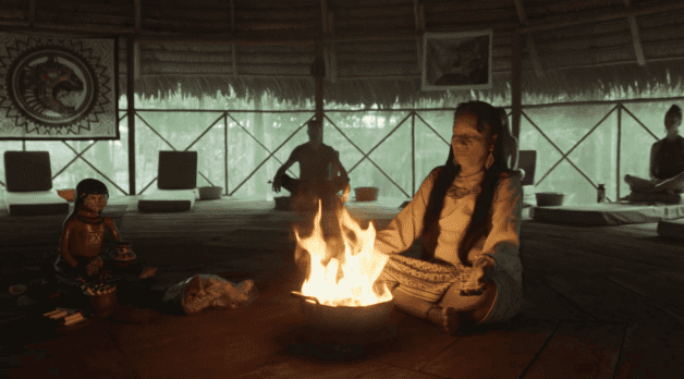 A woman sits near. small fire inside of a hut.