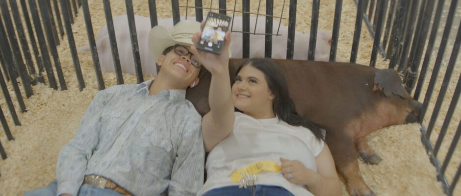 Two high school students take a selfie with two pigs.