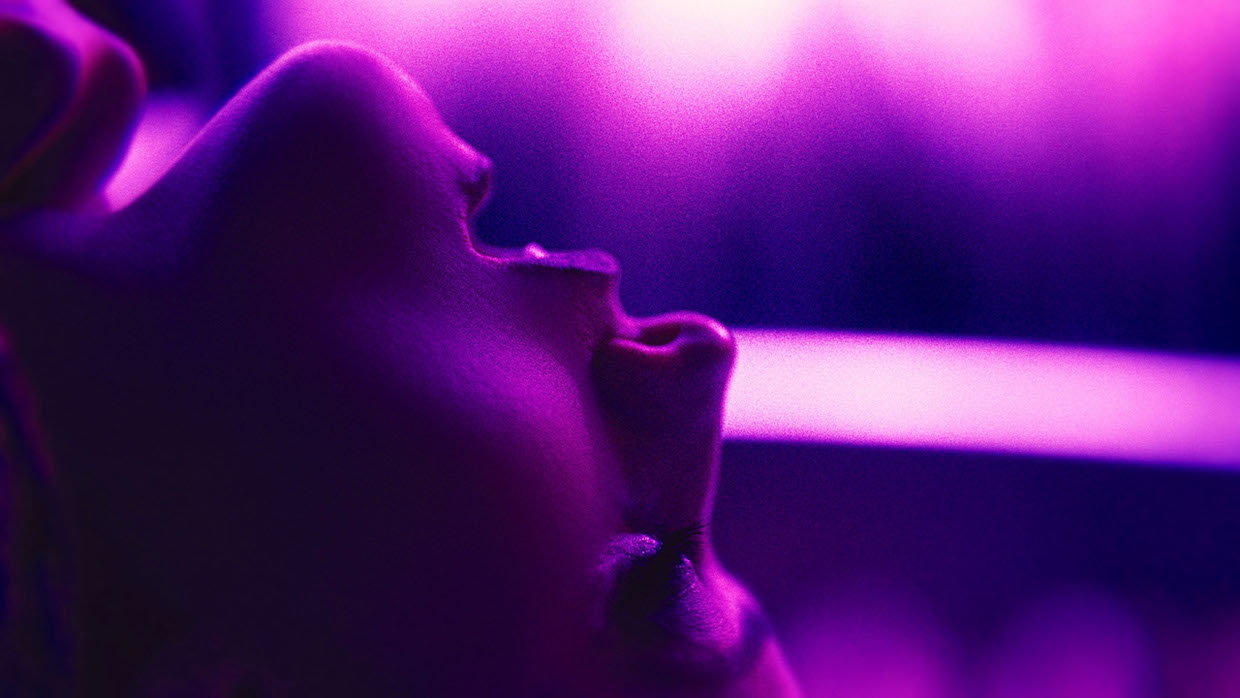 A close-up of a woman's head tilted back with her mouth open; the image is drenched in purple light.