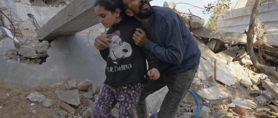 A Palestinian man holds a young girl amid rubble