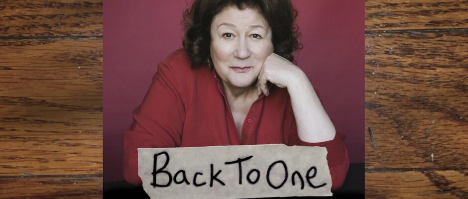 A middle-aged white woman with brown hair and a red top -- the actress Margo Martindale, leaning forward with her chin on her hand.