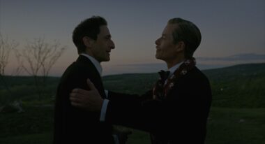 Two men stand on a mountain before a sunset.