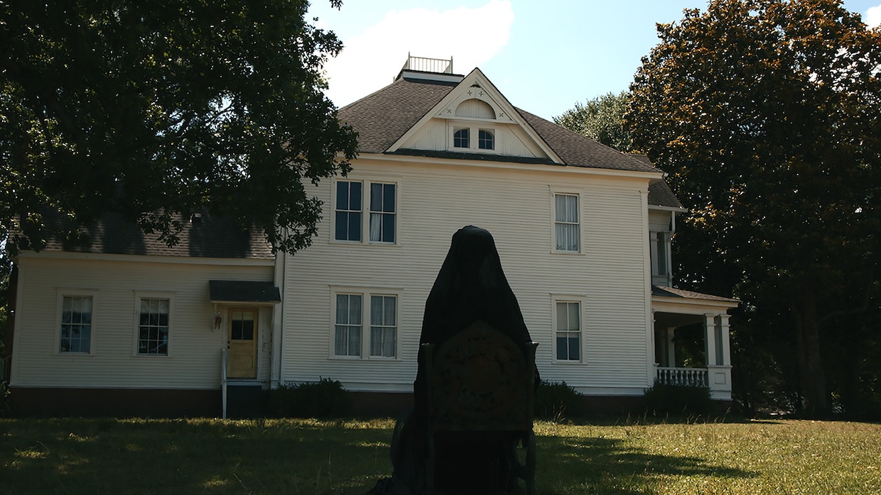 A woman in a full black veil stands outside a house in daylight.
