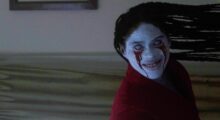 A pale humanoid leans to the side, grinning widely as blood drips from its eyes.