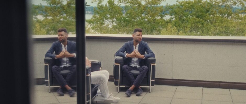 A man in a business casual suit sits in a chair on an outside patio.