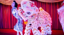 A woman and a Chinese dragon costume stand onstage.