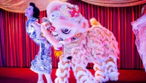 A woman and a Chinese dragon costume stand onstage.