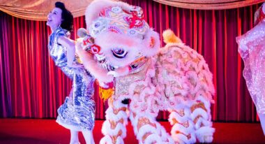 A woman and a Chinese dragon costume stand onstage.