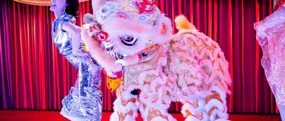 A woman and a Chinese dragon costume stand onstage.