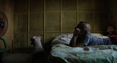 A boy rests on a bed with his dog next to him in a dark room.