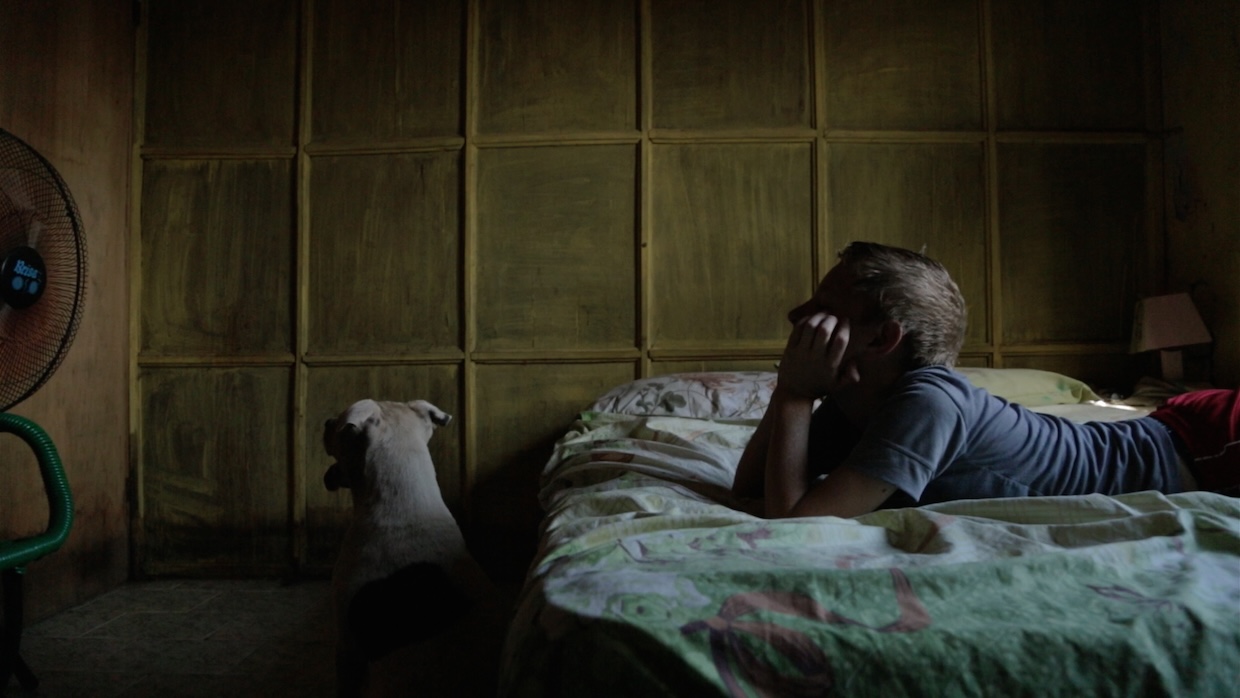 The-Prince-of-Nanawa_CIL_2469644 | Filmmaker Magazine A boy rests on a bed with his dog next to him in a dark room.