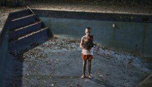A young boy stands in an empty pool at night while holding a dog.