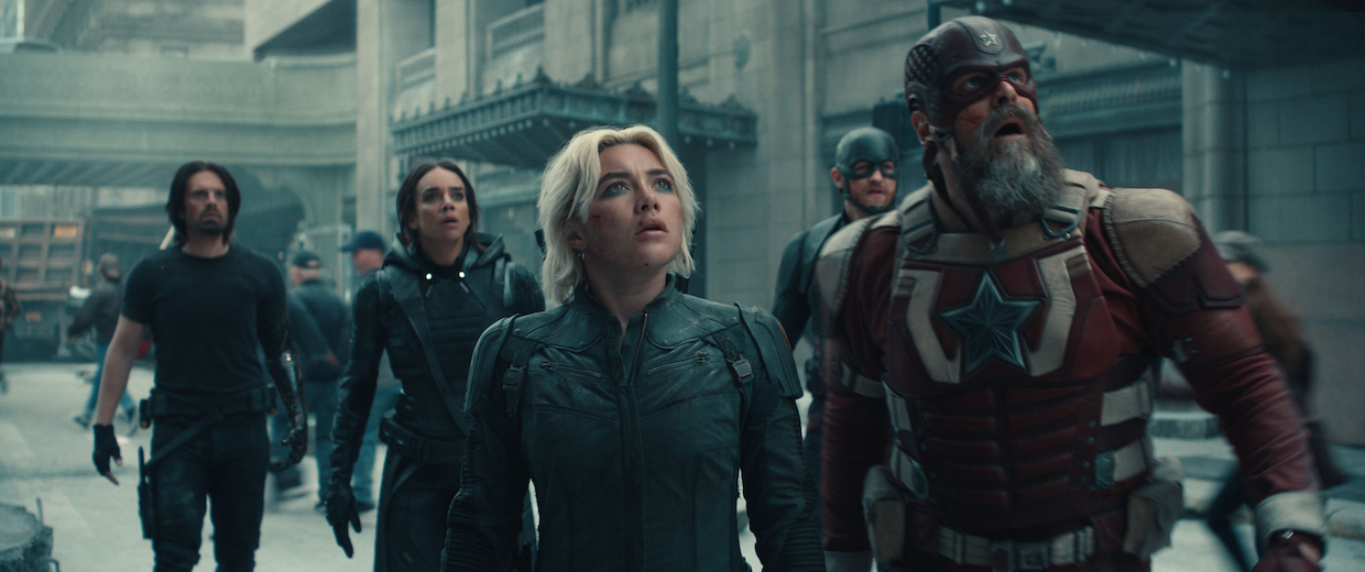 A group of superheroes on a street look alarmed.