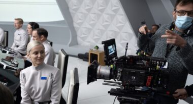 A cinematographer wearing a face mask stands nexts to a camera on a spaceship set.