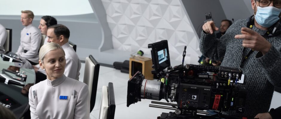 A cinematographer wearing a face mask stands nexts to a camera on a spaceship set.