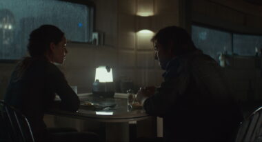 Two people sit at a table in a dimly lit room.