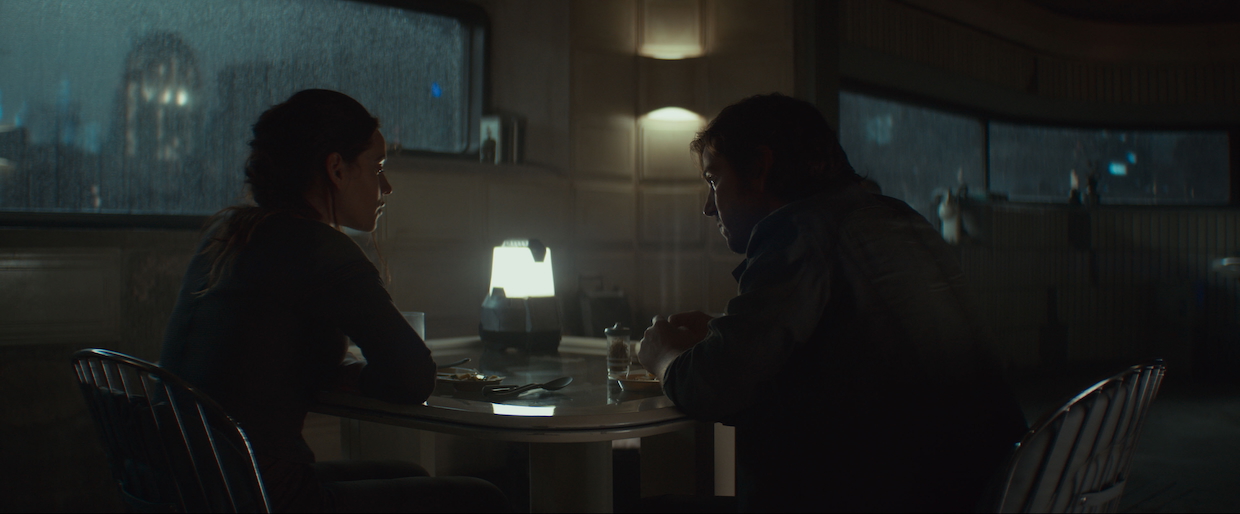 Two people sit at a table in a dimly lit room.